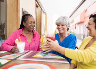 Multiracial senior women having fun cheering with healthy drinks at brunch restaurant