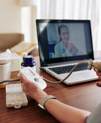 Woman measuring her blood pressure with electronic tonometer at home under control of virtual doctor